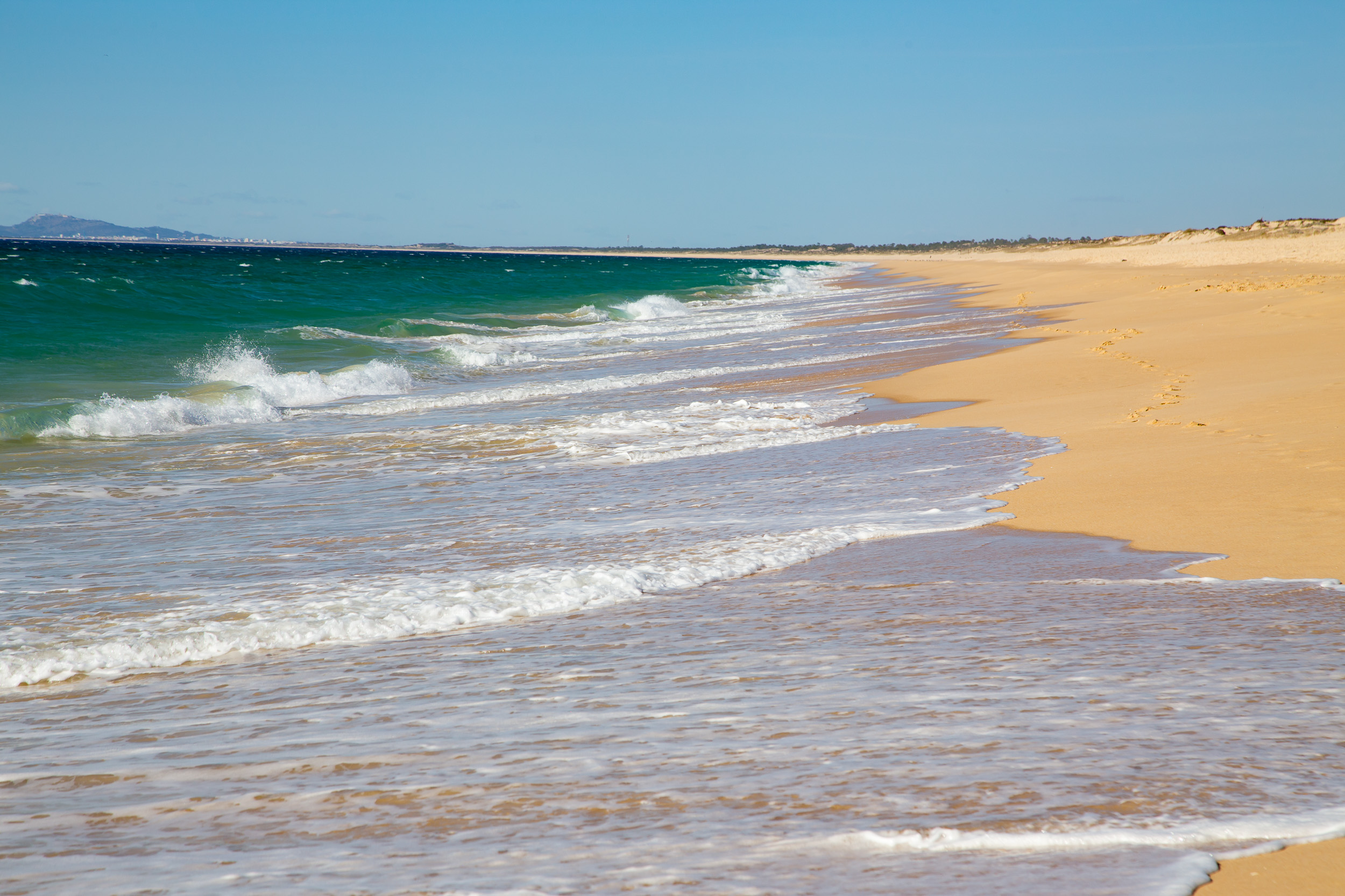 Blick entlang des endlos weiten, leeren Sandstrandes von Comporta mit den Wellen des Atlantiks.