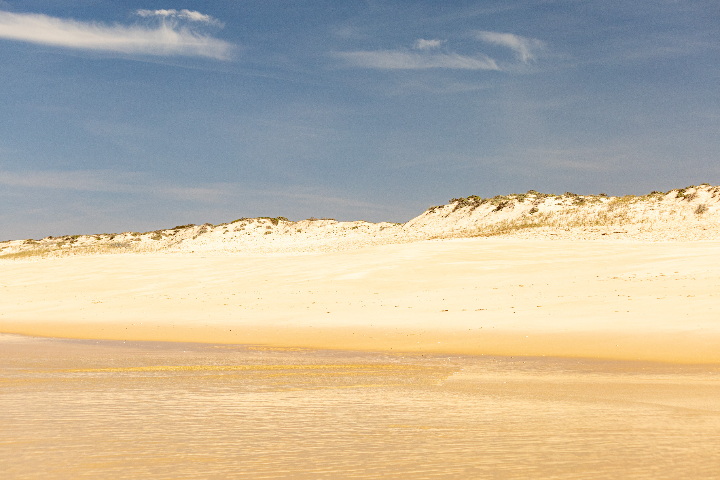 Heller Sandstrand und sanfte Dünen unter strahlend blauem Himmel am Praia do Carvalhal.