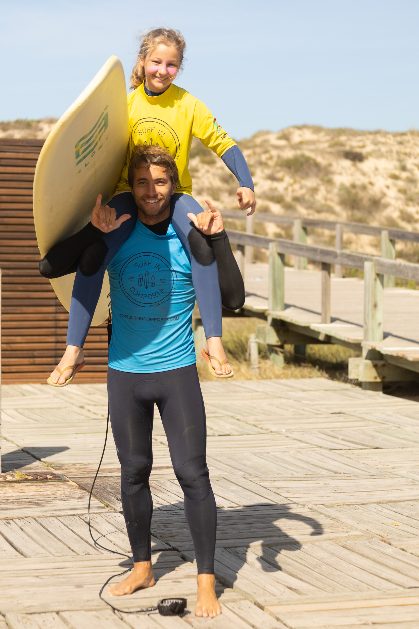 Un moniteur de surf en combinaison rit et plaisante avec des enfants sur la plage.