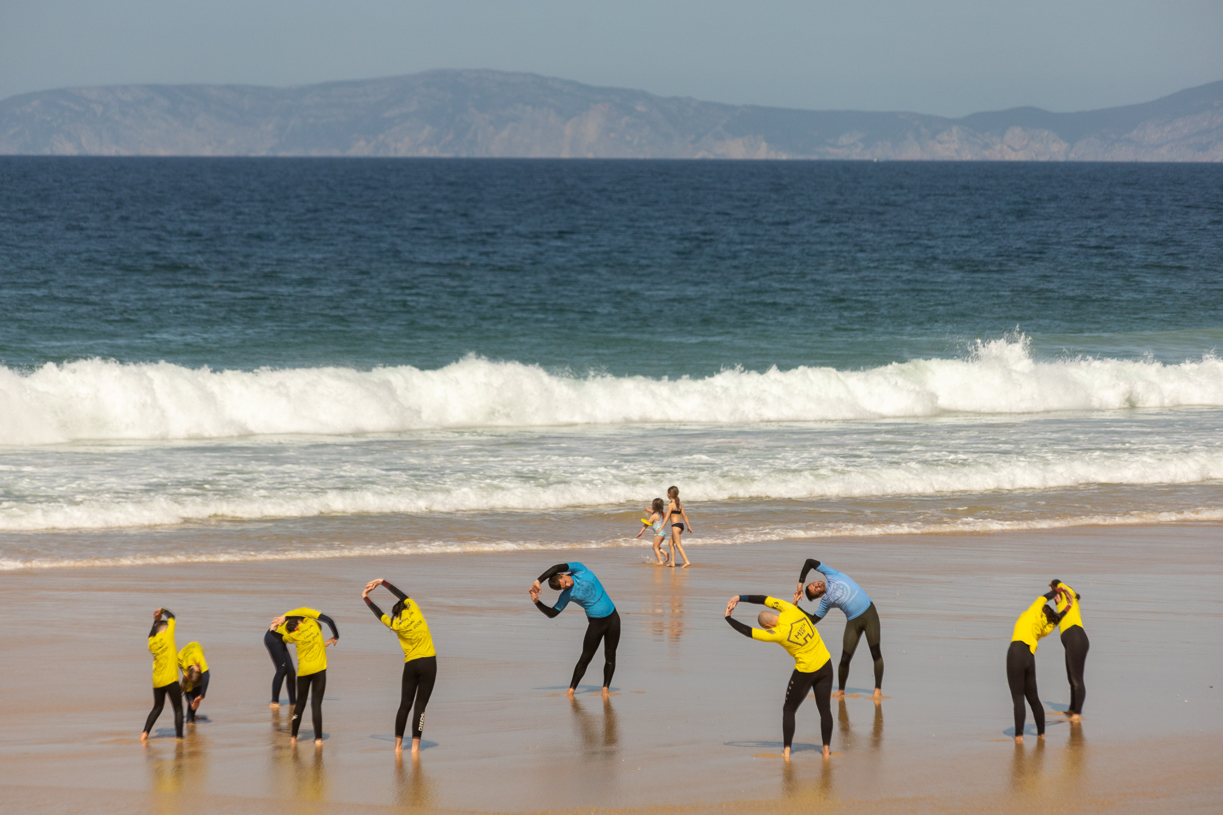 Un groupe d'élèves de surf s'échauffe ensemble dans le sable devant les planches de surf.