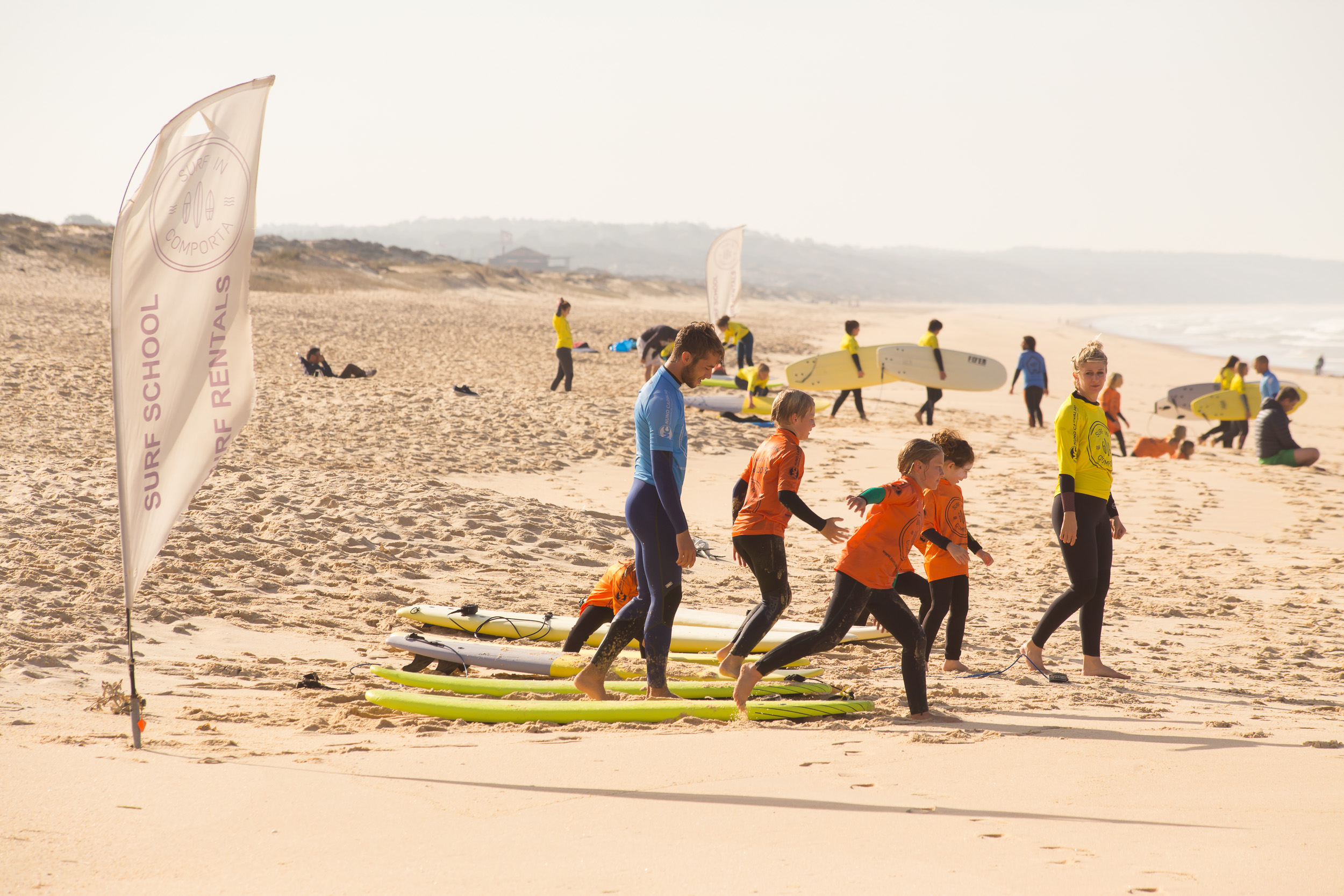 Surfschüler laufen mit ihren Brettern ins Wasser in eine durch Flaggen markierte Zone.