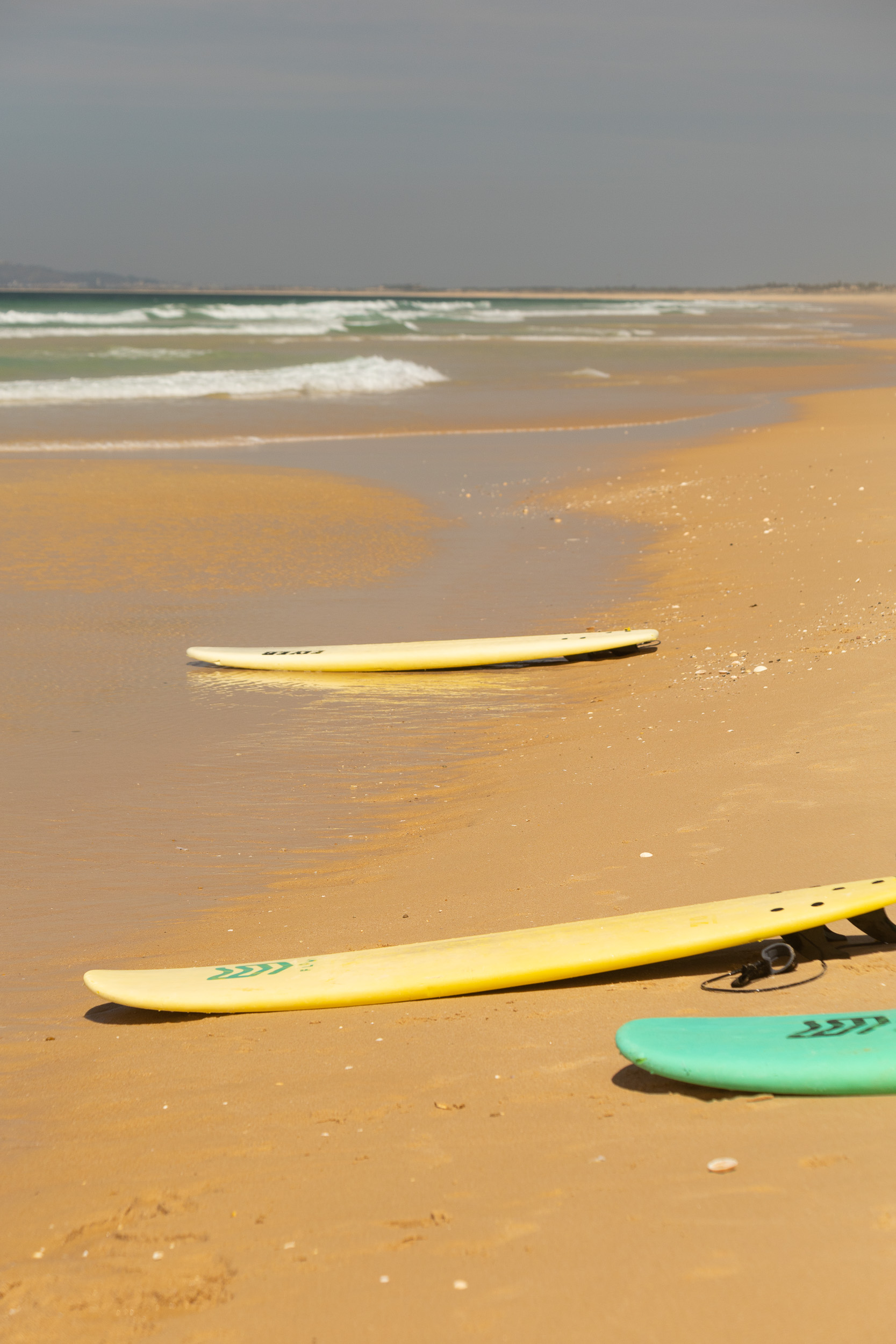 Plusieurs planches de surf colorées sont posées à plat sur le sable lors d'une courte pause.