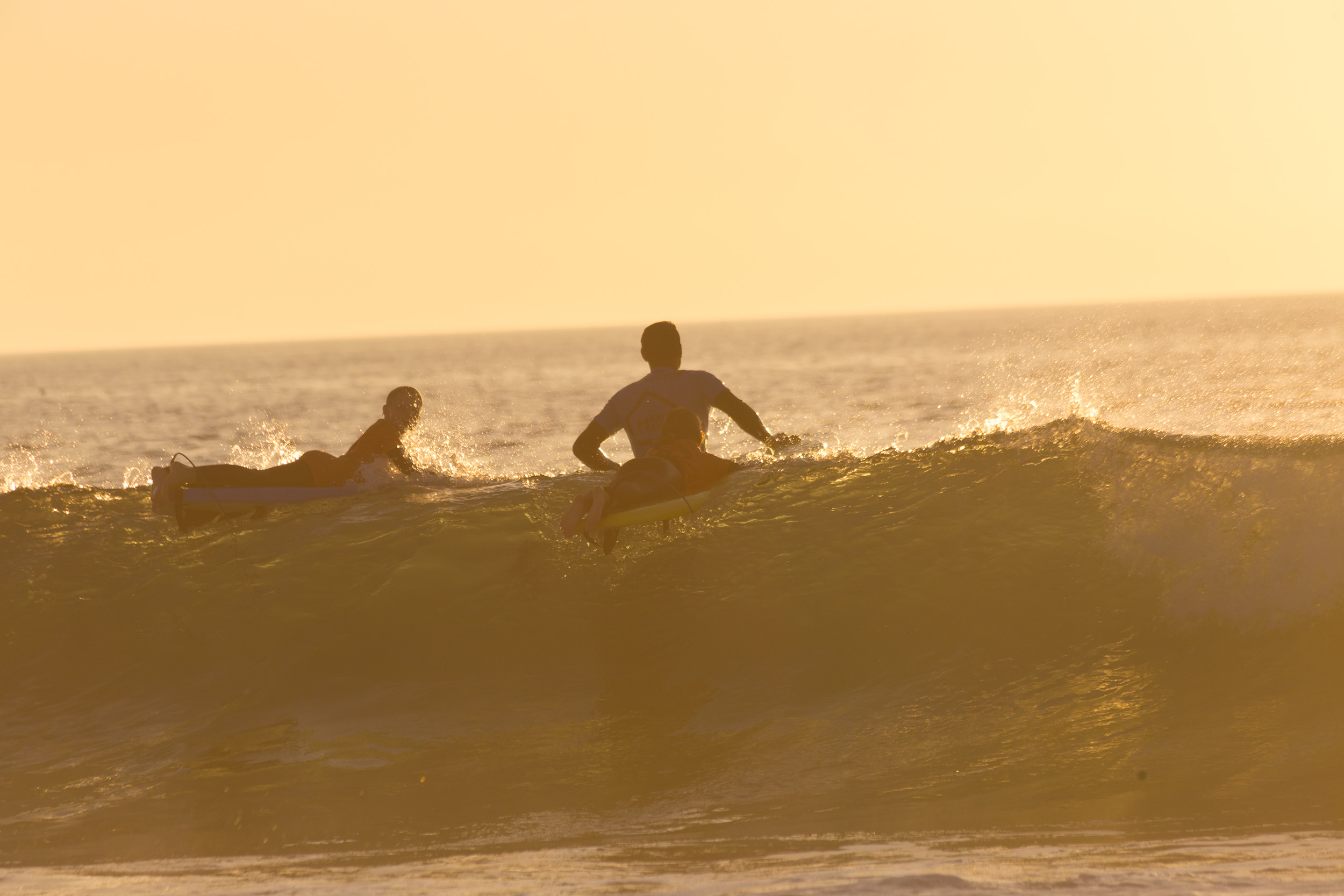 Un surfeur glisse sur une vague dans la lumière chaude du soleil couchant.