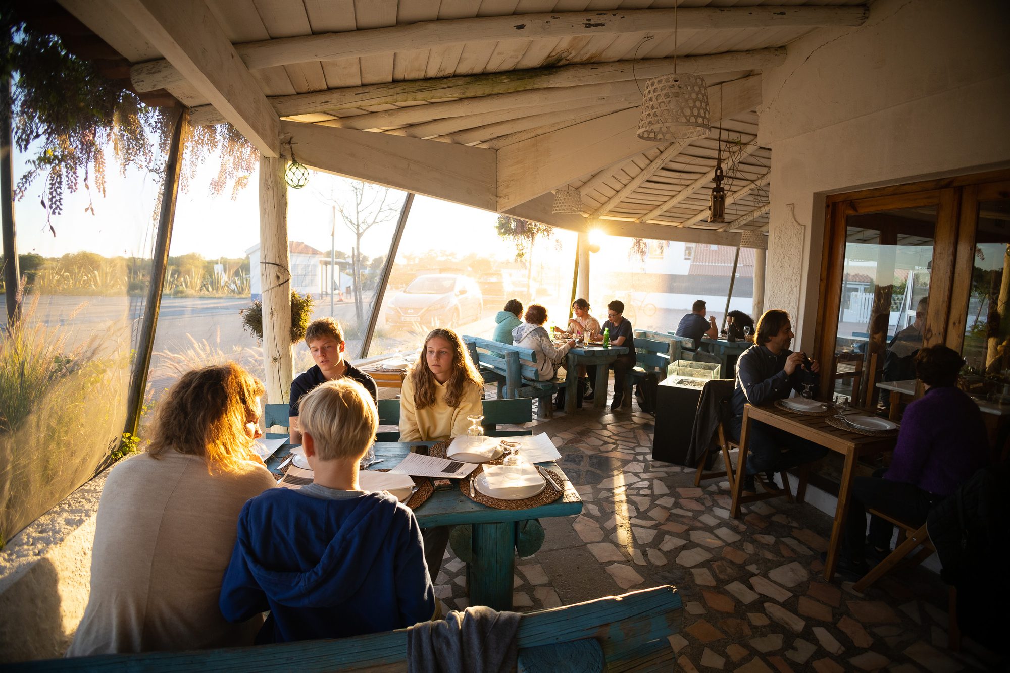 A covered outdoor terrace with several tables in the warm light of the late afternoon.